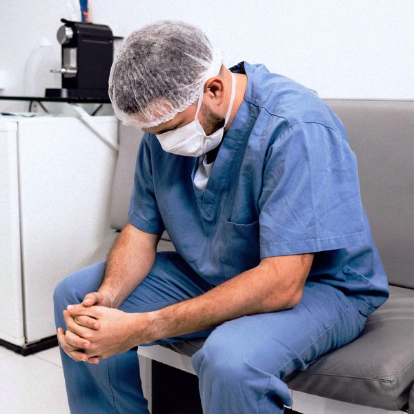 Tired looking doctor resting on bench with hands together